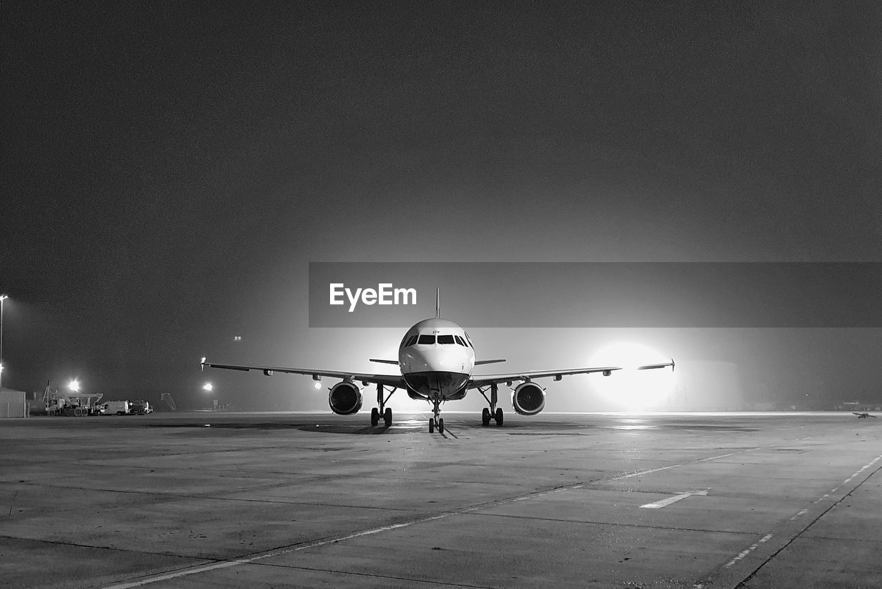 Airplane on airport runway against clear sky at night