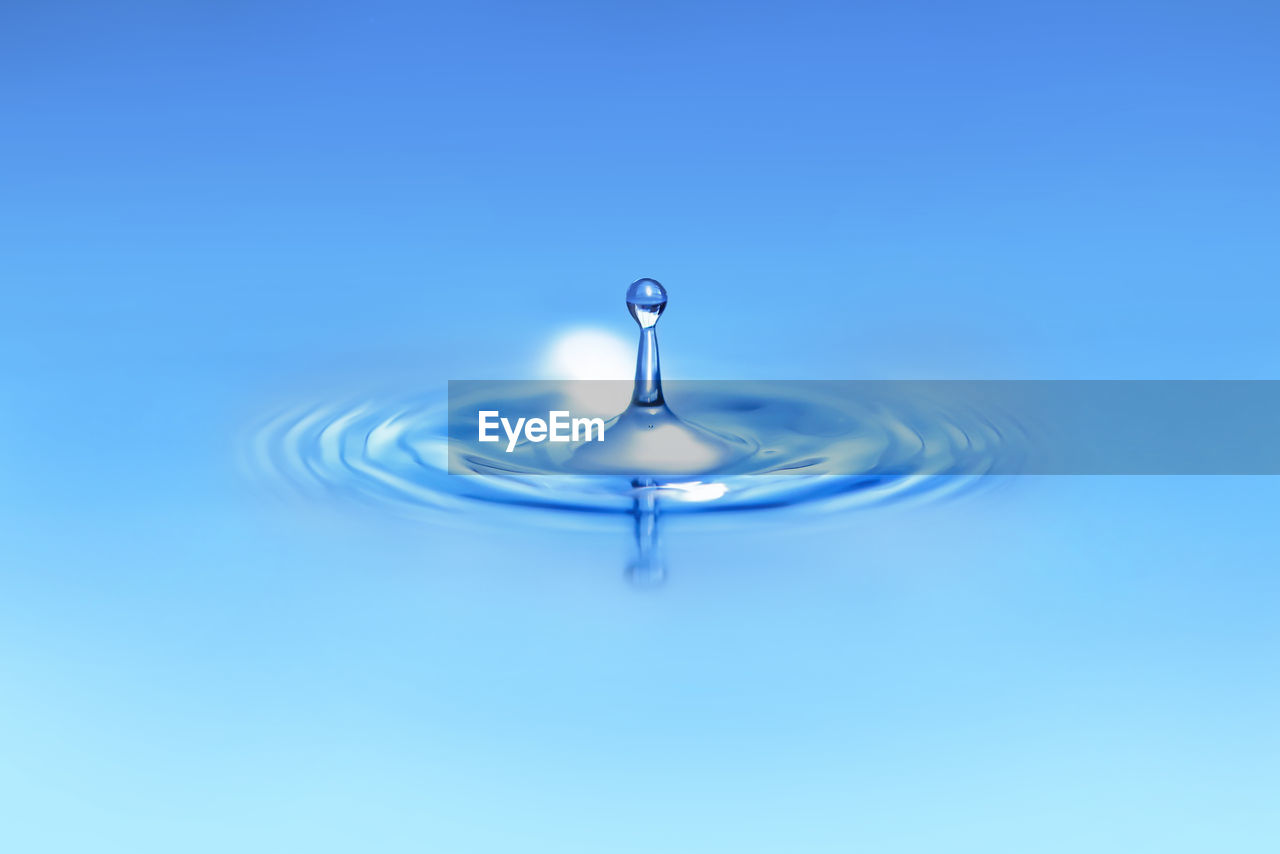 Close-up of drop falling on water against blue background
