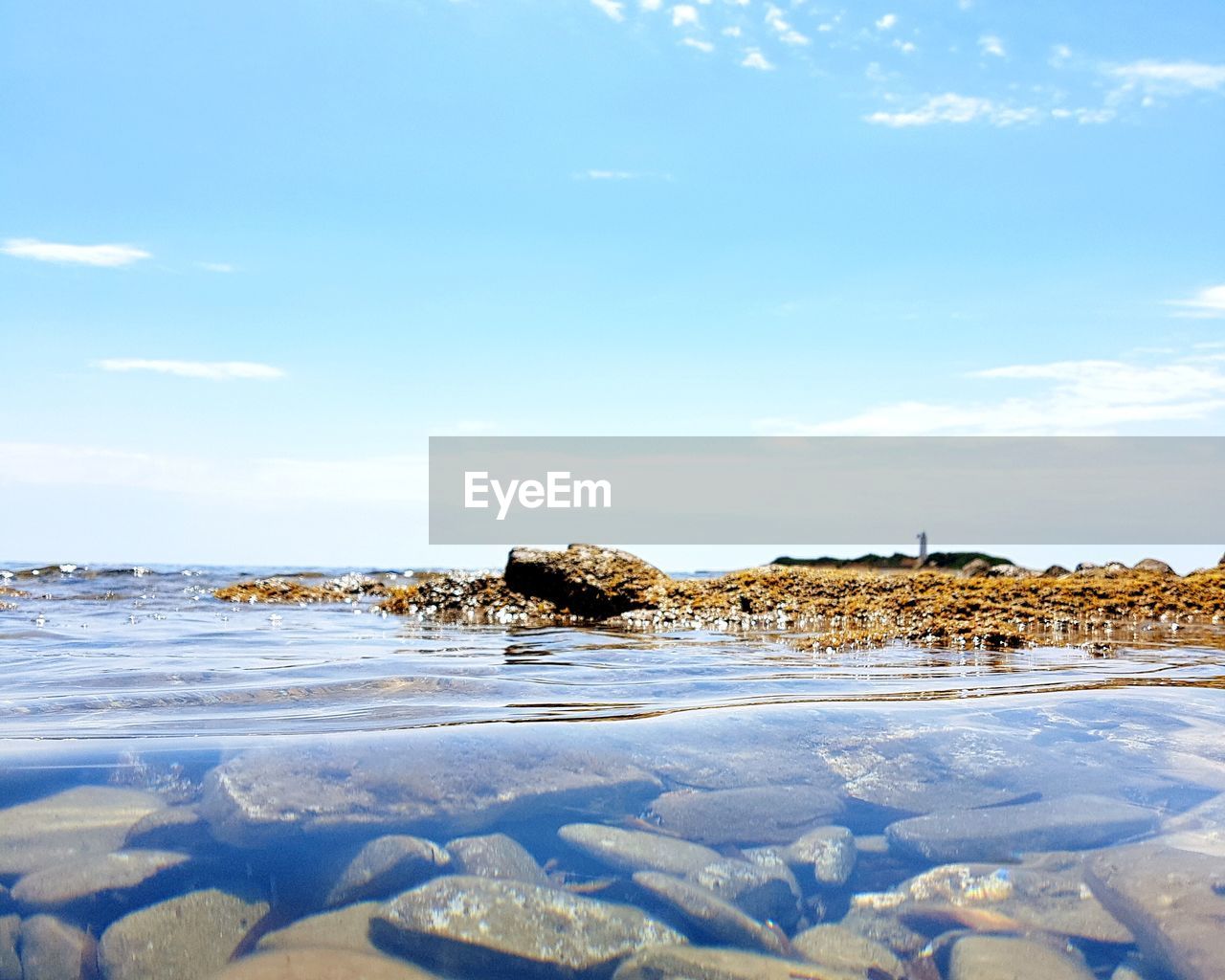 ROCKS BY SEA AGAINST BLUE SKY