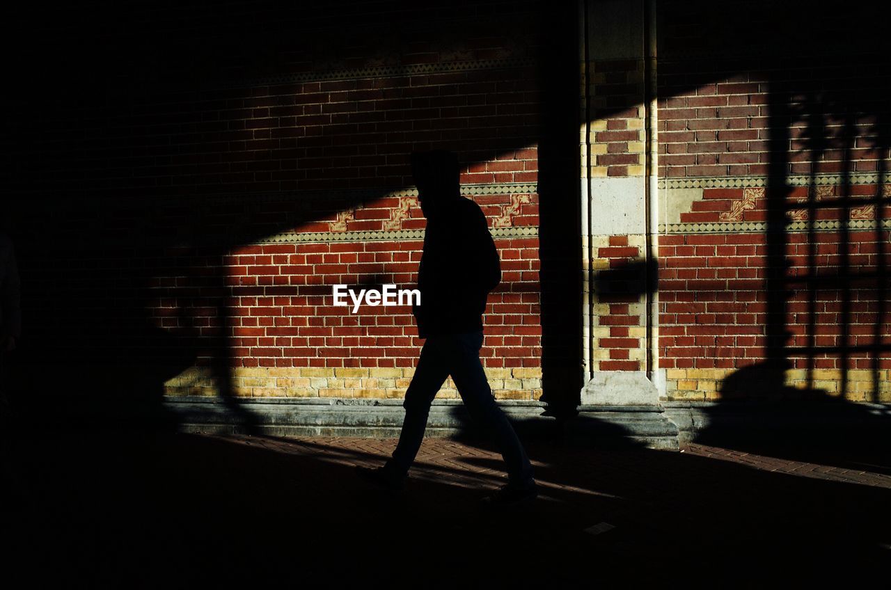 Silhouette man walking by wall