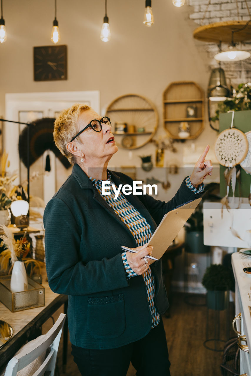 Senior female owner holding clipboard while doing inventory at decor shop