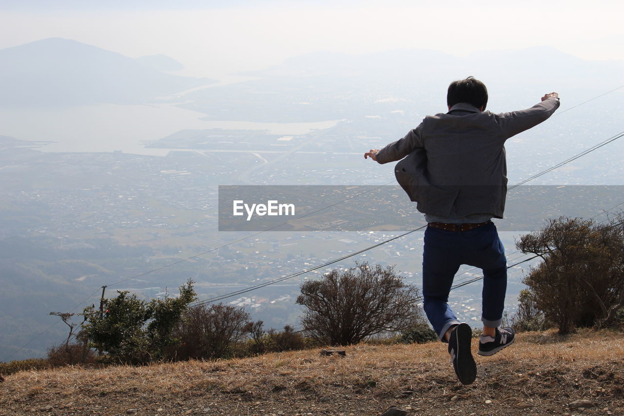 REAR VIEW OF MAN STANDING ON MOUNTAIN