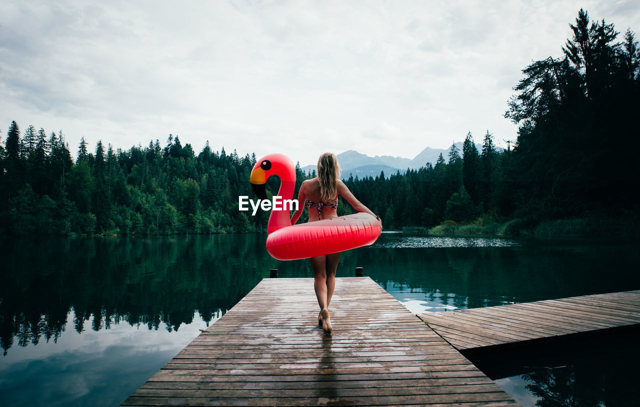 WOMAN ON PIER AMIDST LAKE AGAINST SKY