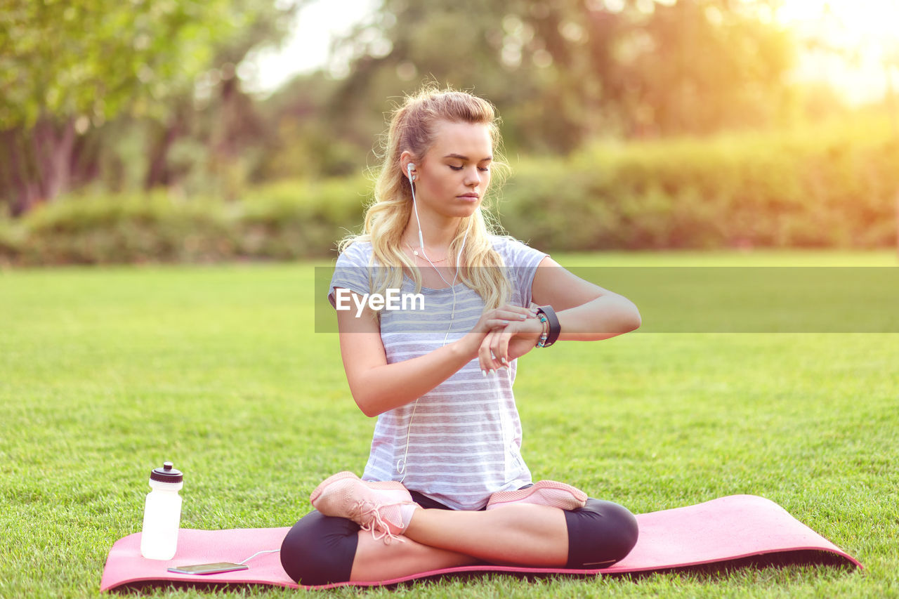 Mindful young woman checking pulse while doing yoga meditation workout at home backyard