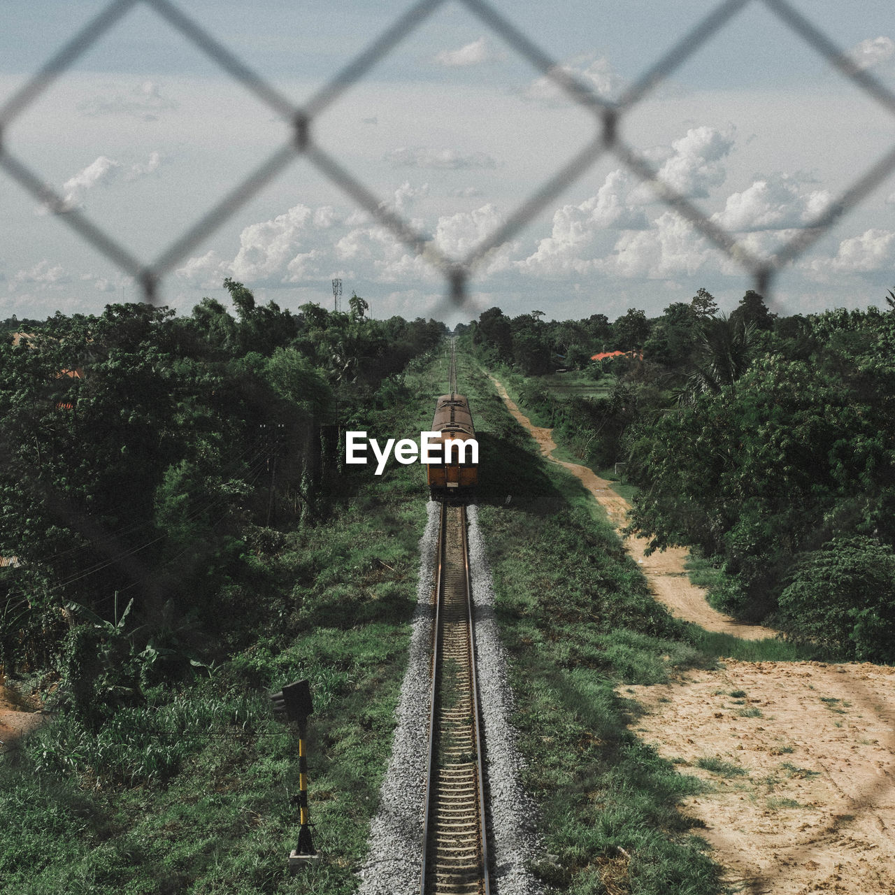 High angle view of train moving amidst trees against sky seen through fence