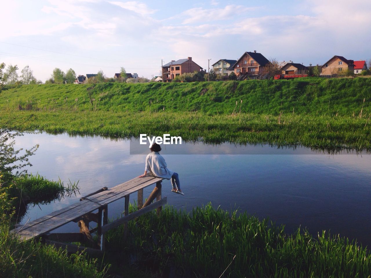 Rear view of woman sitting on pier against river