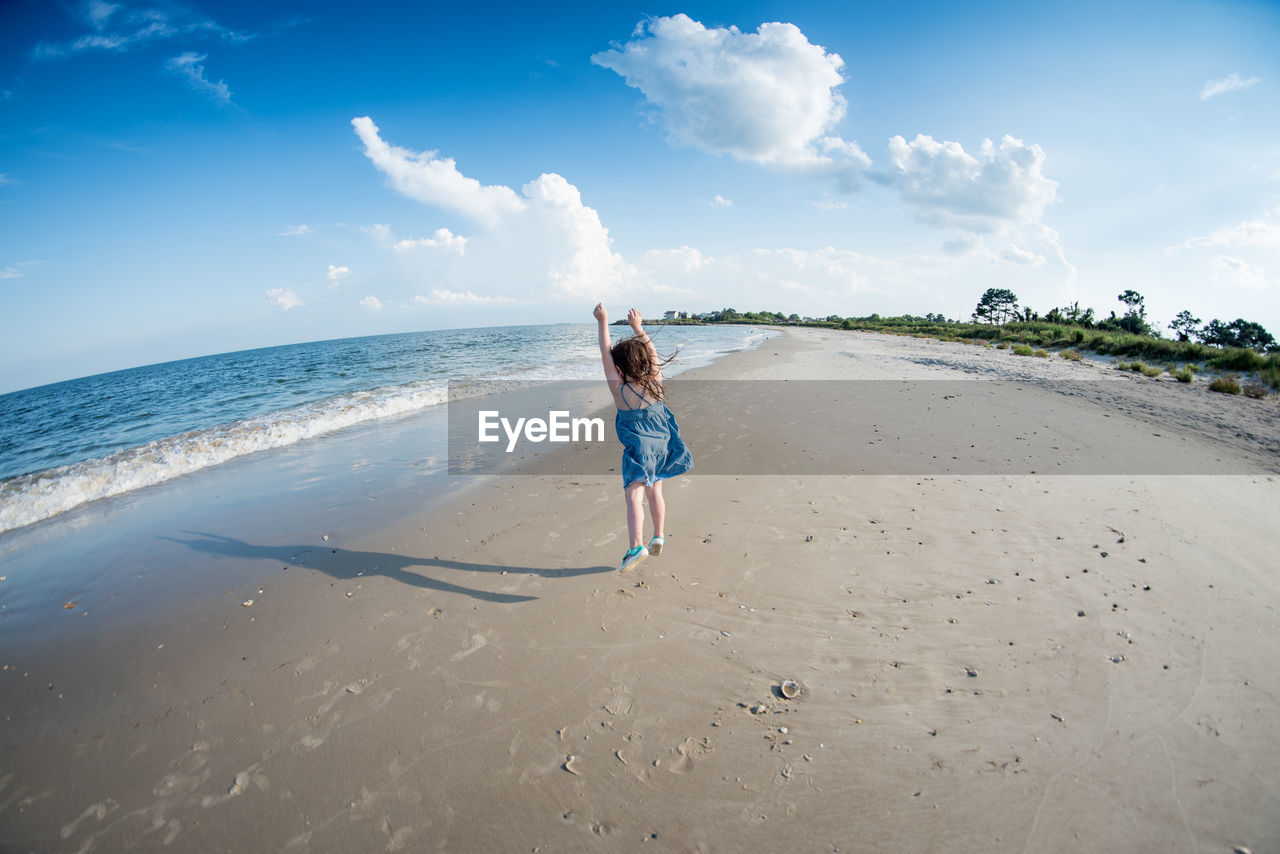 Rear view of girl jumping on beach against sky