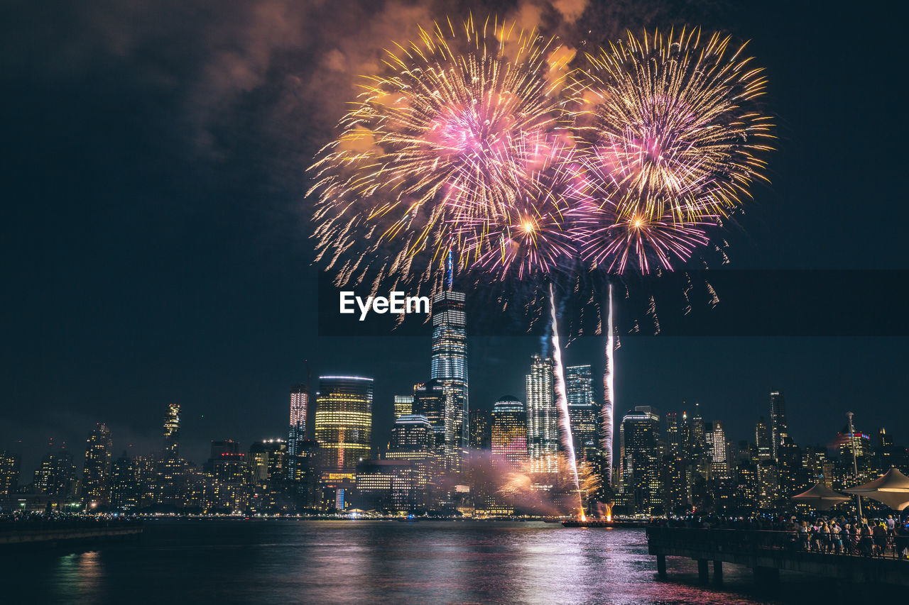 Low angle view of firework display over river in city at night