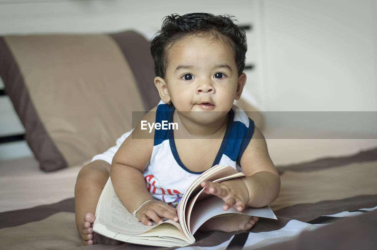 Portrait of baby with book sitting at home