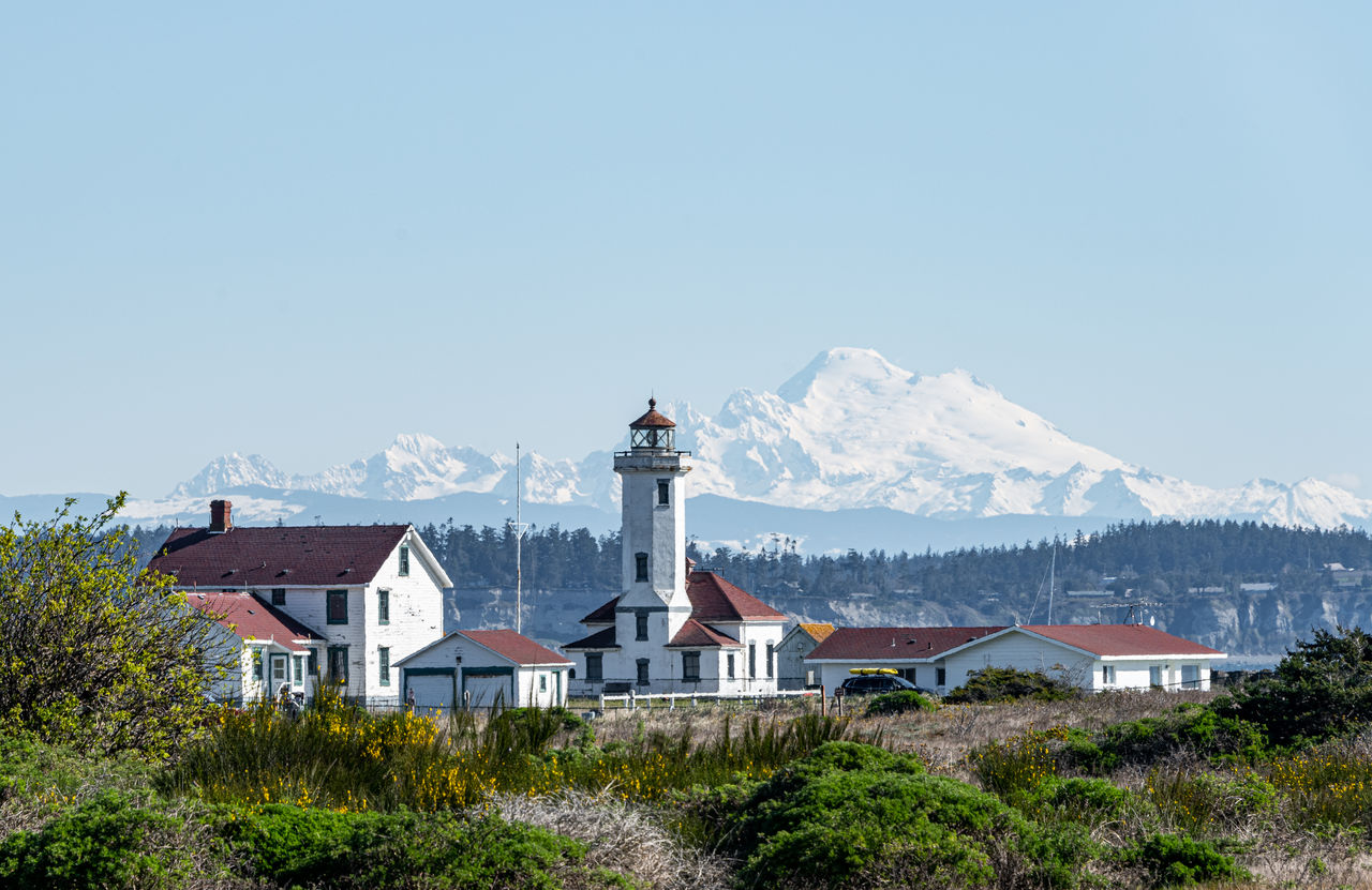 Lighthouse by buildings against clear blue sky