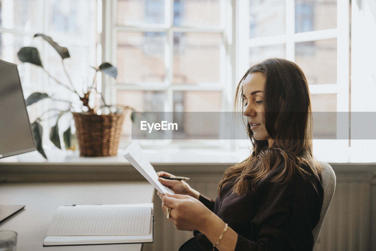 Side view of businesswoman examining document sitting at office