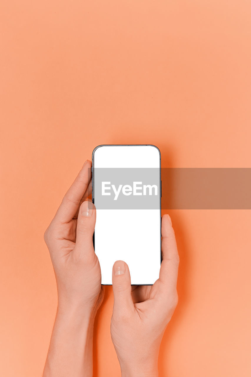 cropped hands of woman using smart phone against yellow background