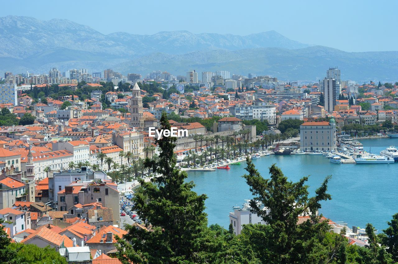 HIGH ANGLE VIEW OF TOWNSCAPE BY SEA AGAINST SKY