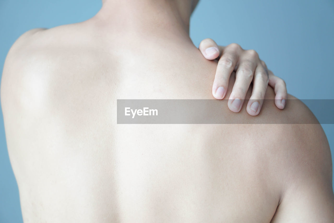 Rear view of shirtless man touching shoulder in pain