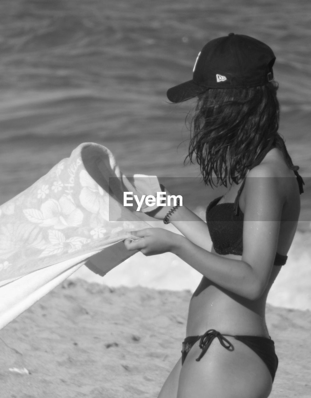 Side view of woman in bikini holding towel while standing at beach