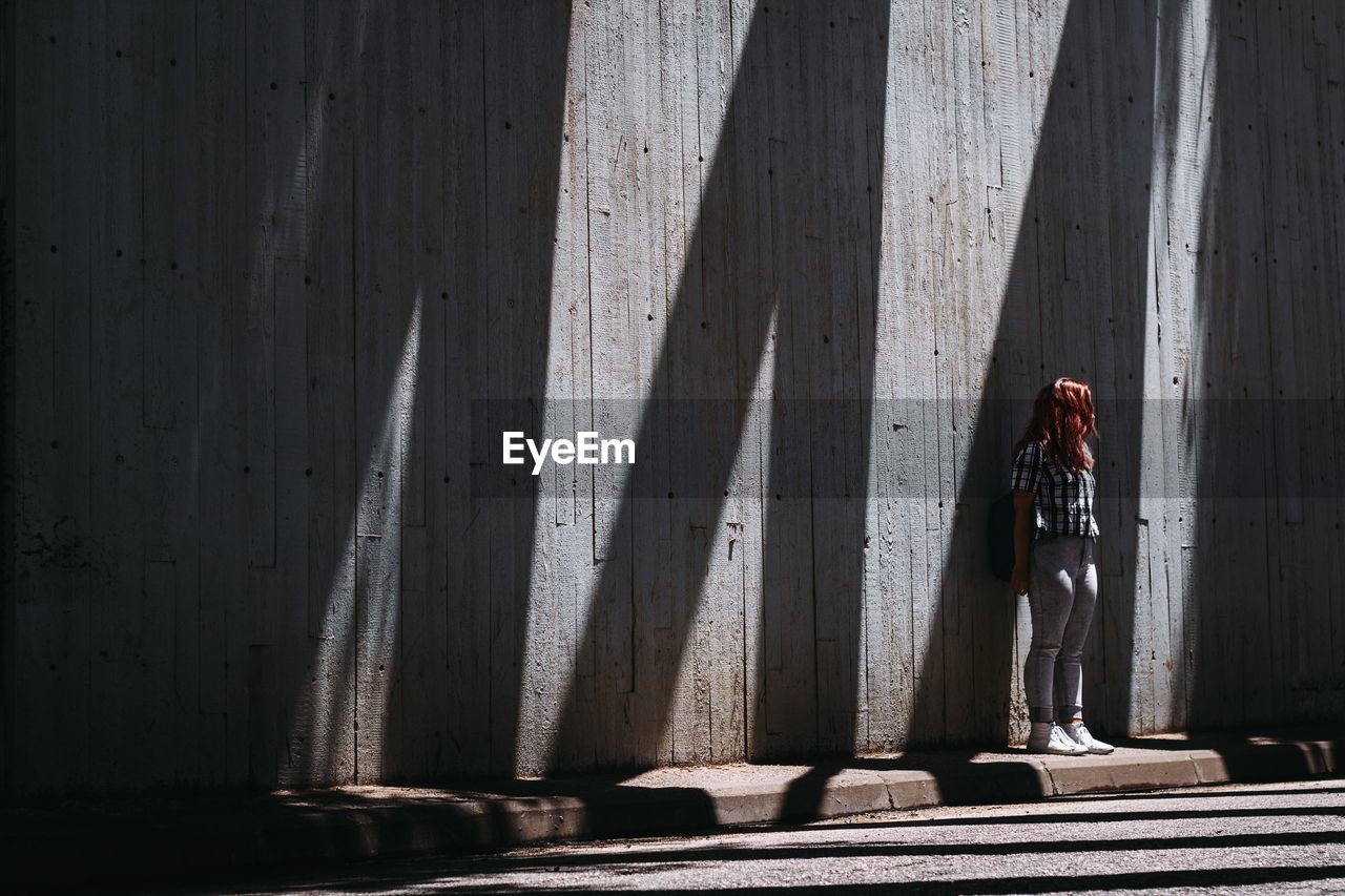 Woman standing on footpath against wall