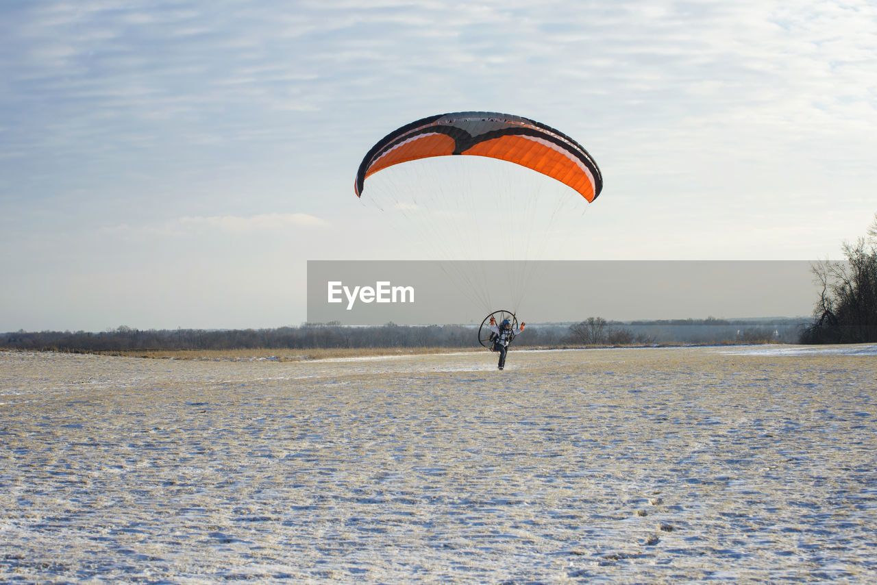 Young man motor paragliding over field against sky