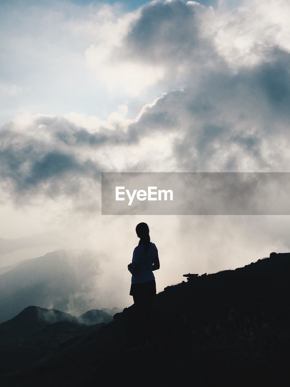 Woman standing on silhouette field against cloudy sky