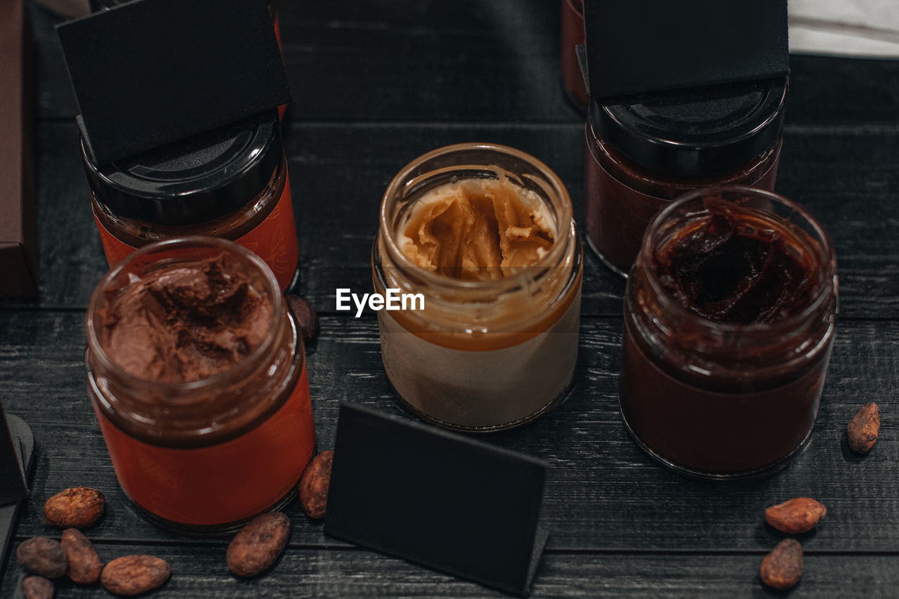 Handmade chocolate spread or nougat cream on glass jar on wooden rustic background with cacao beans.