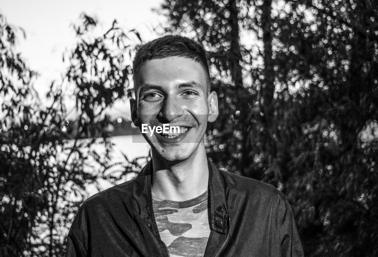 Portrait of smiling young man standing by trees