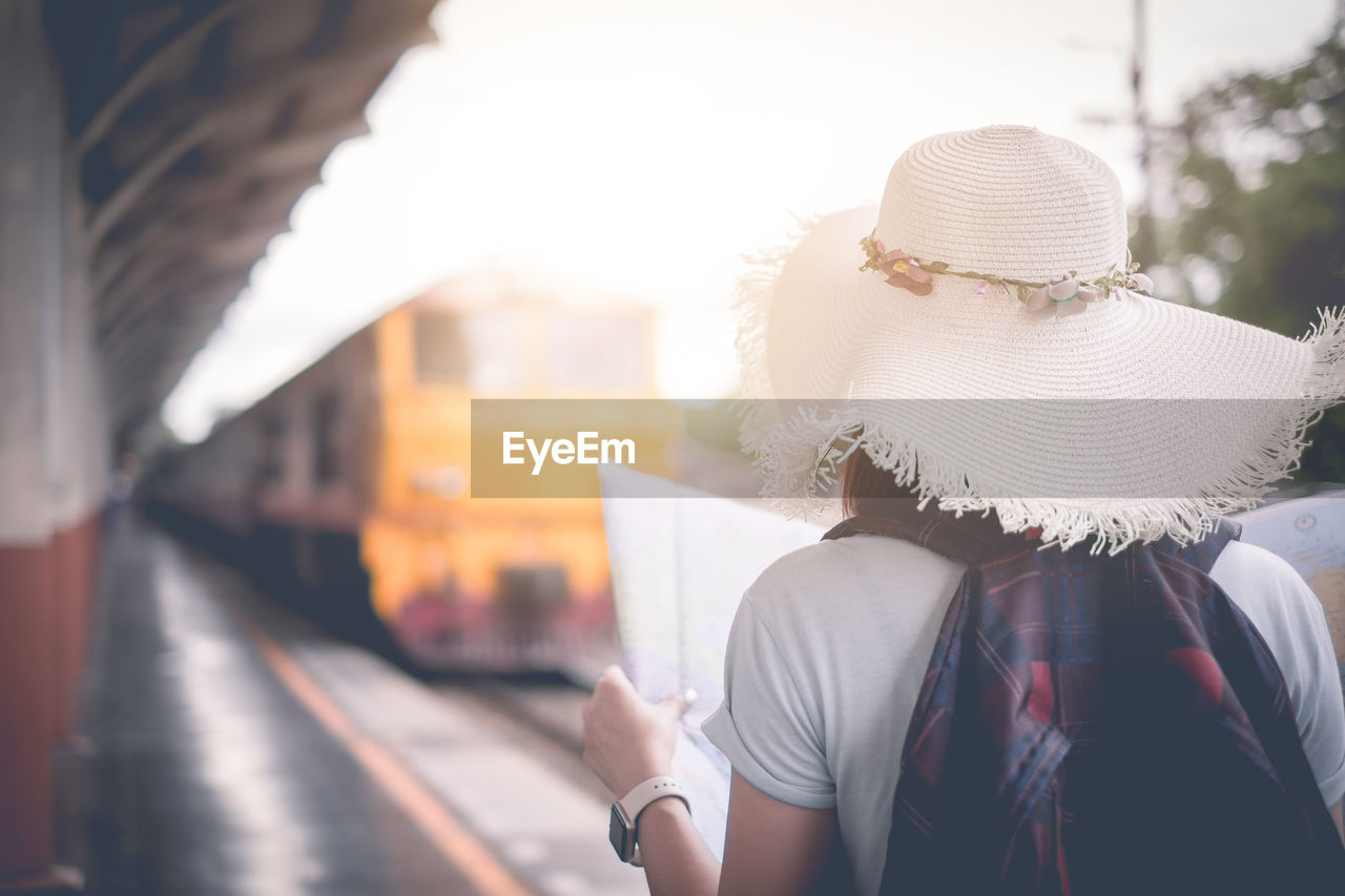 Rear view of woman holding map while standing at railroad station platform in city