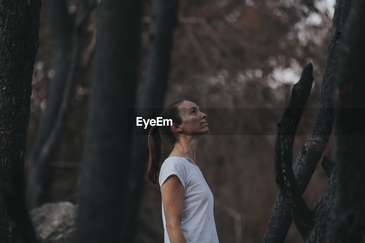 Thoughtful woman standing amidst burnt trees in forest