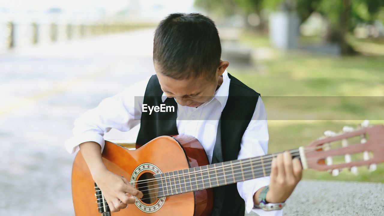 Close-up of boy playing guitar while standing at park