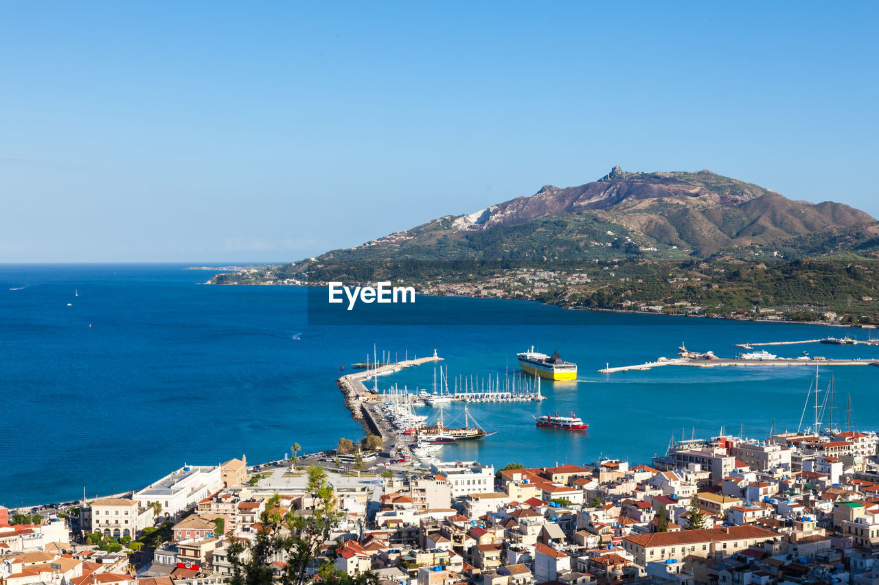 Aerial view of cityscape by sea against blue sky