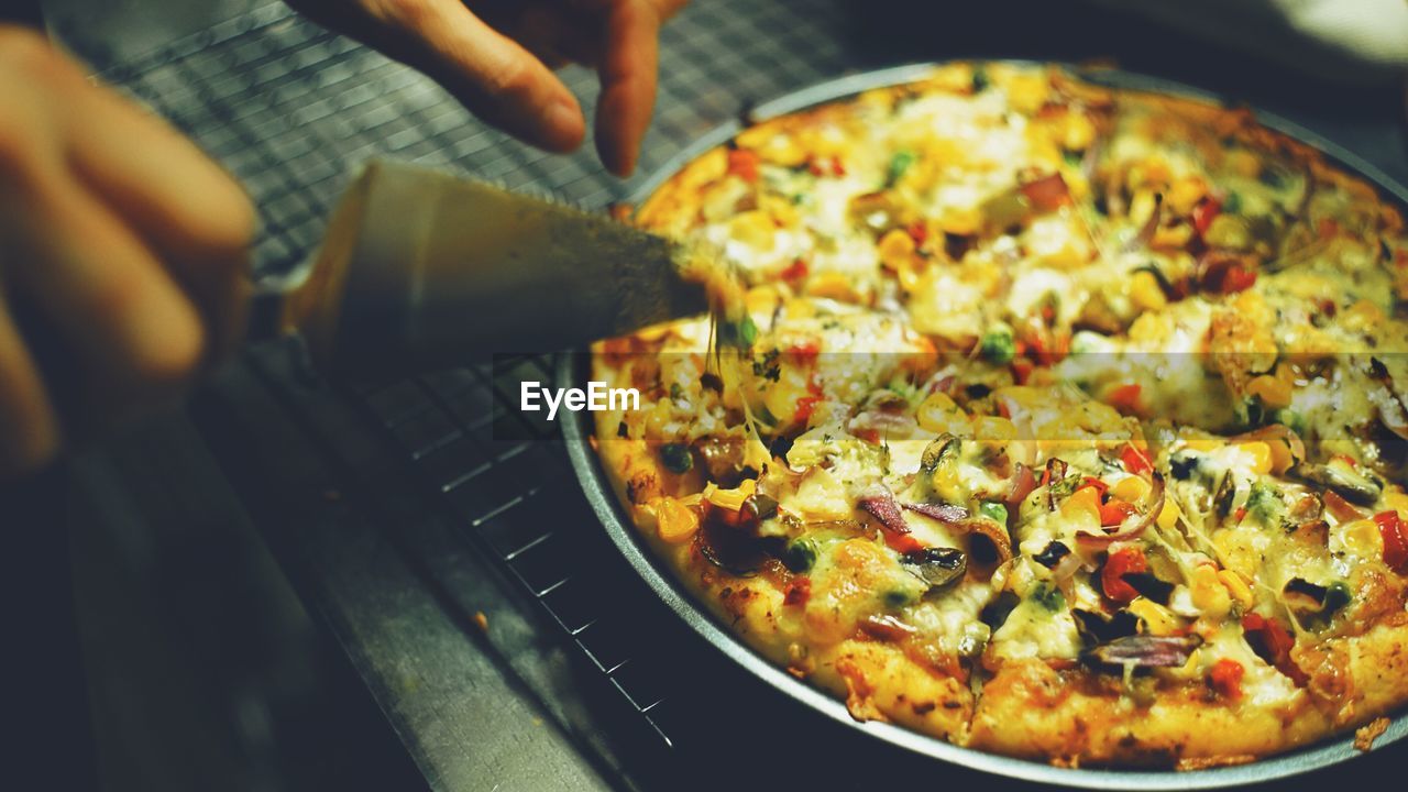 Cropped hands cutting pizza at cooling rack