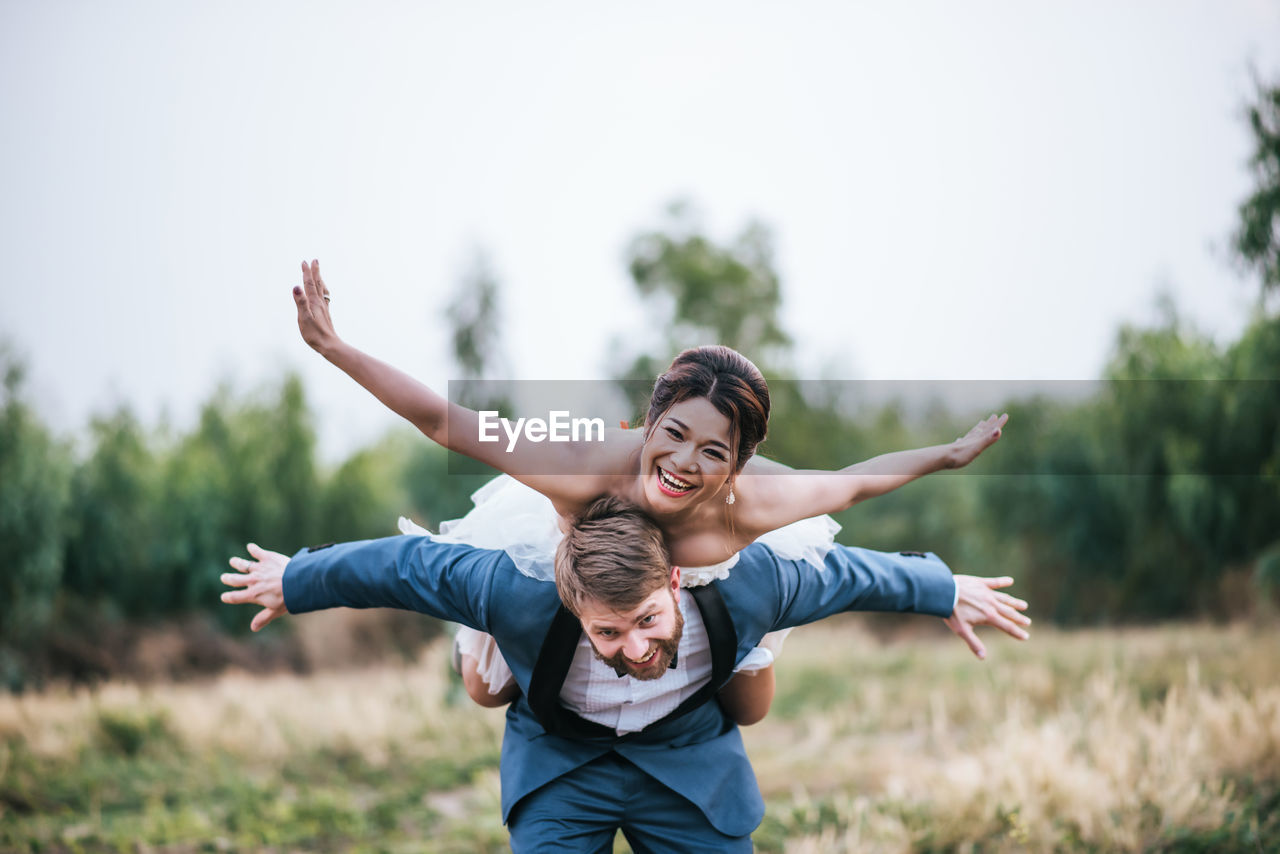 Portrait of smiling man piggybacking woman against sky