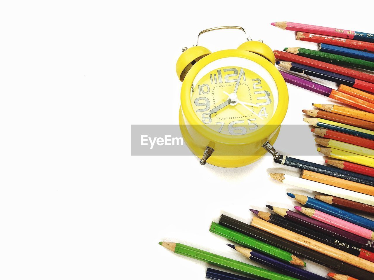 High angle view of colored pencils and alarm clock against white background