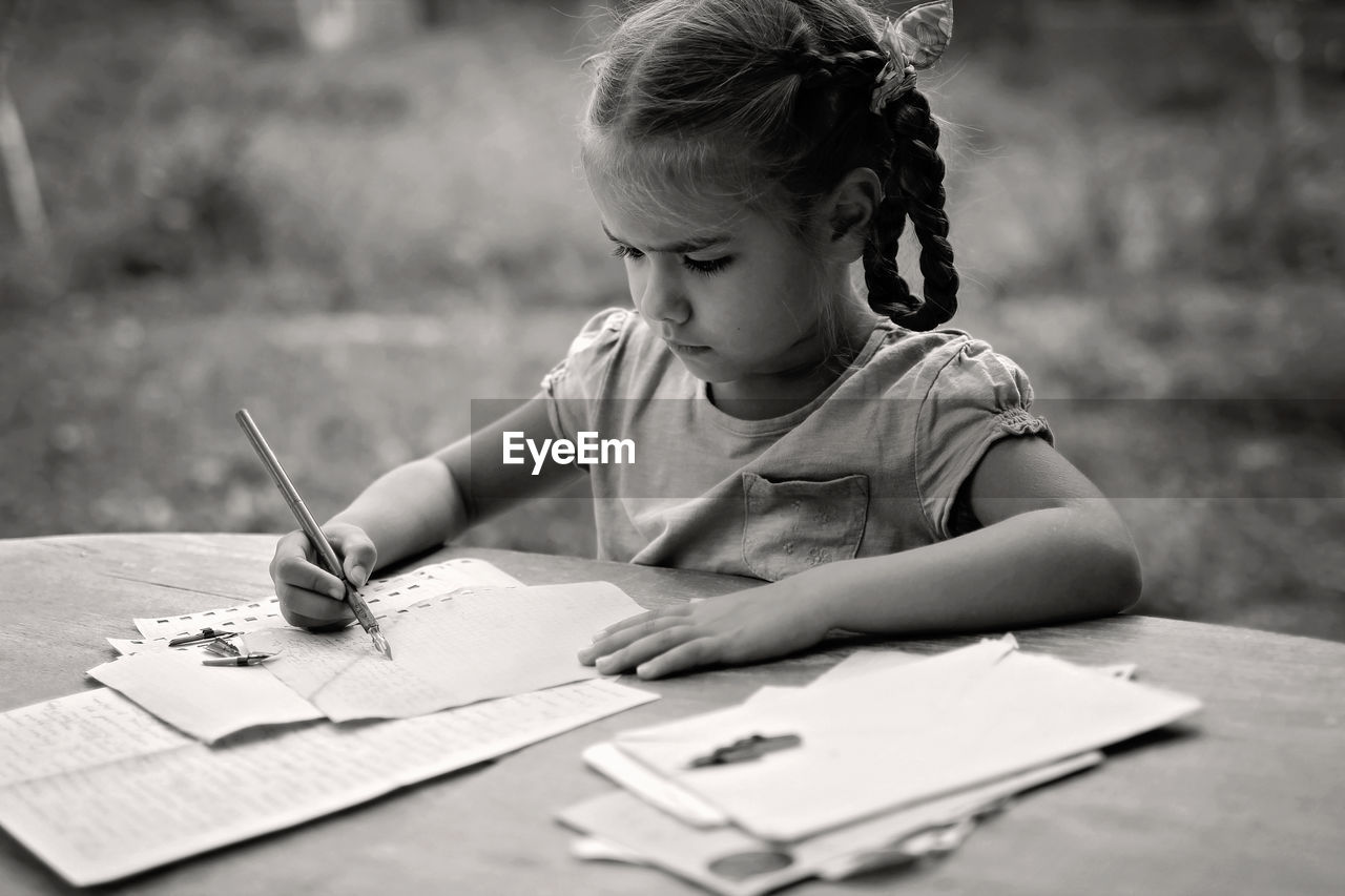 Cute girl drawing on paper while sitting outdoors