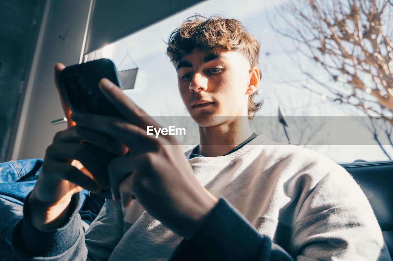 Low angle portrait of trendy teenager boy using mobile phone