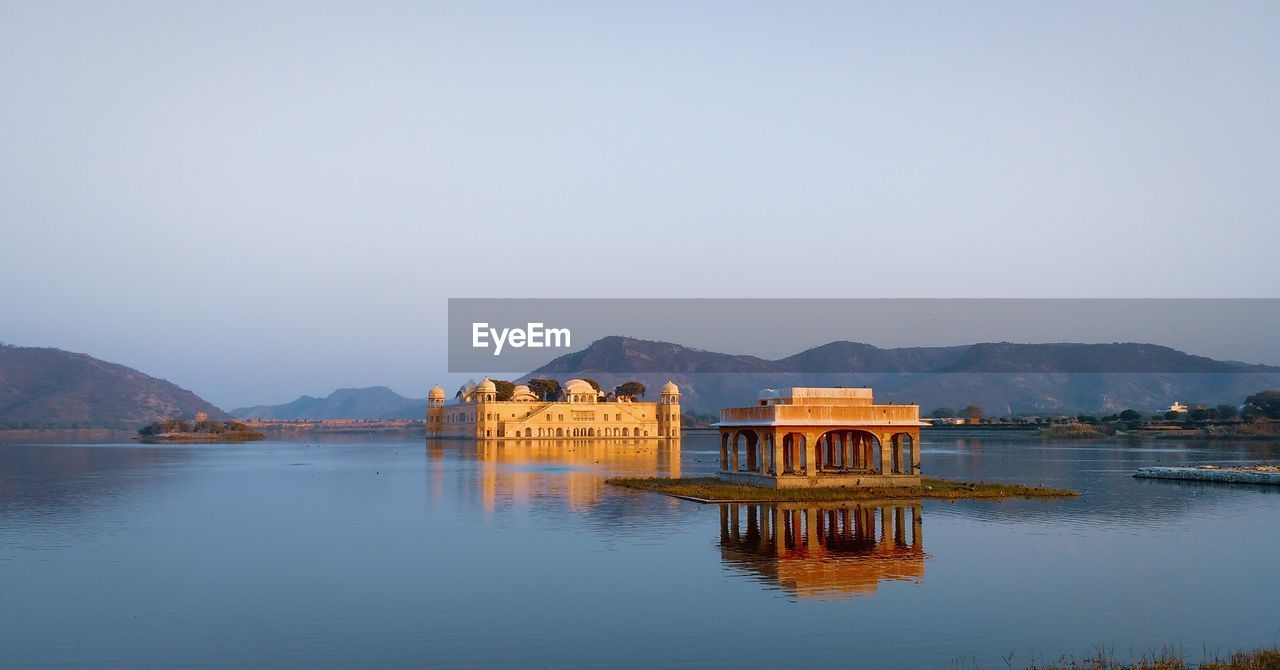 Built structure on lake by mountains against clear sky