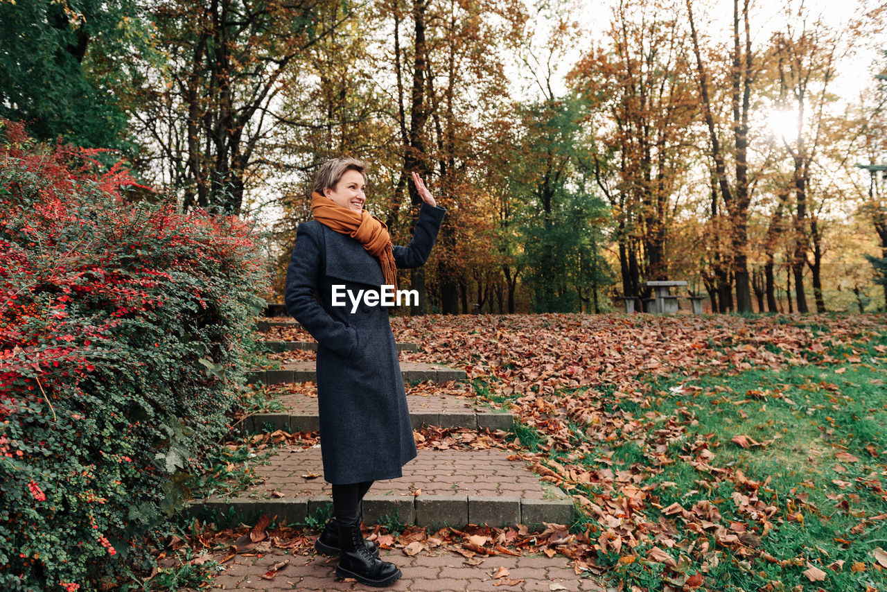 A young woman waves her hand in the fall in the park