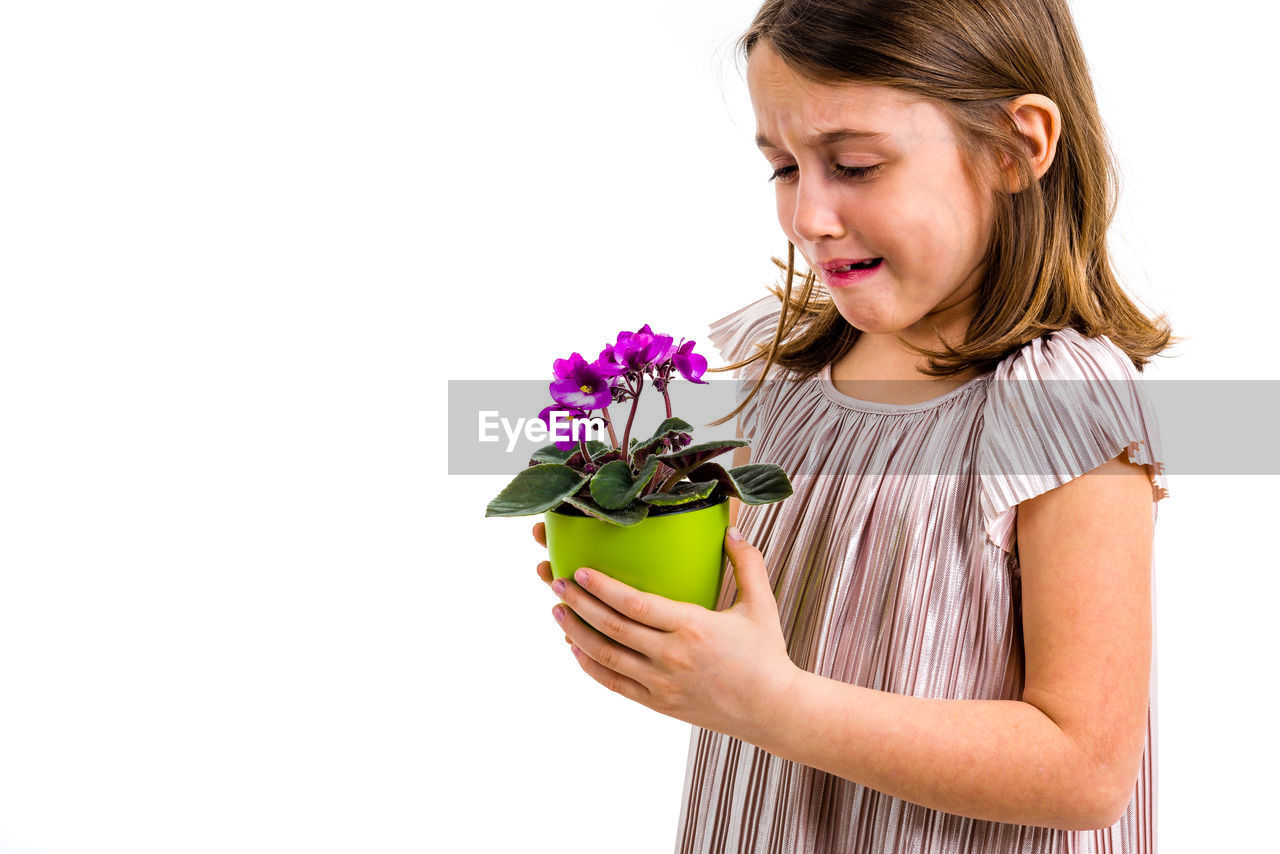 Close-up of sad girl with flower pot standing against white background