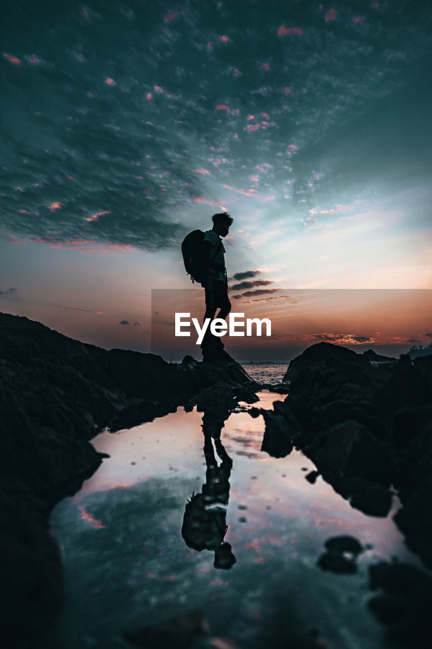 Silhouette man standing on rock against sky during sunset