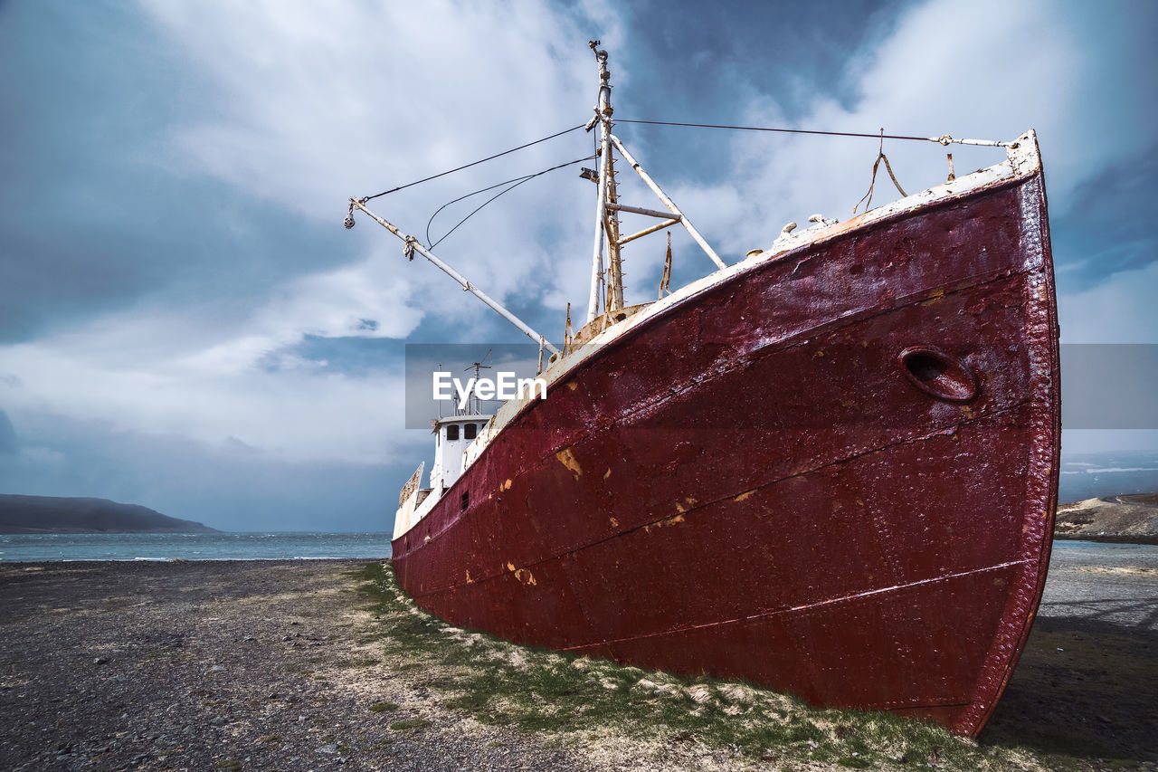 Fishing boat on beach against cloudy sky