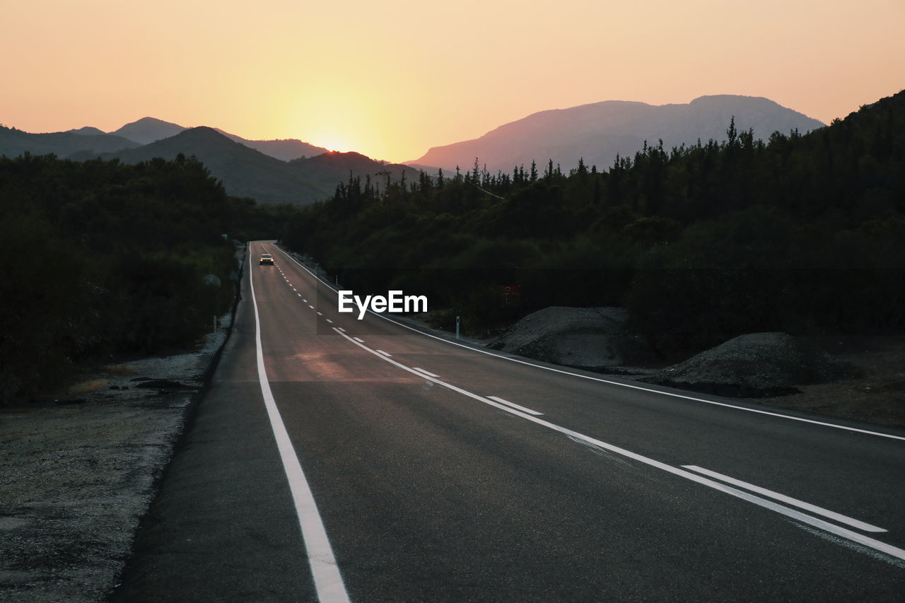 Empty road leading towards mountains against sky during sunset