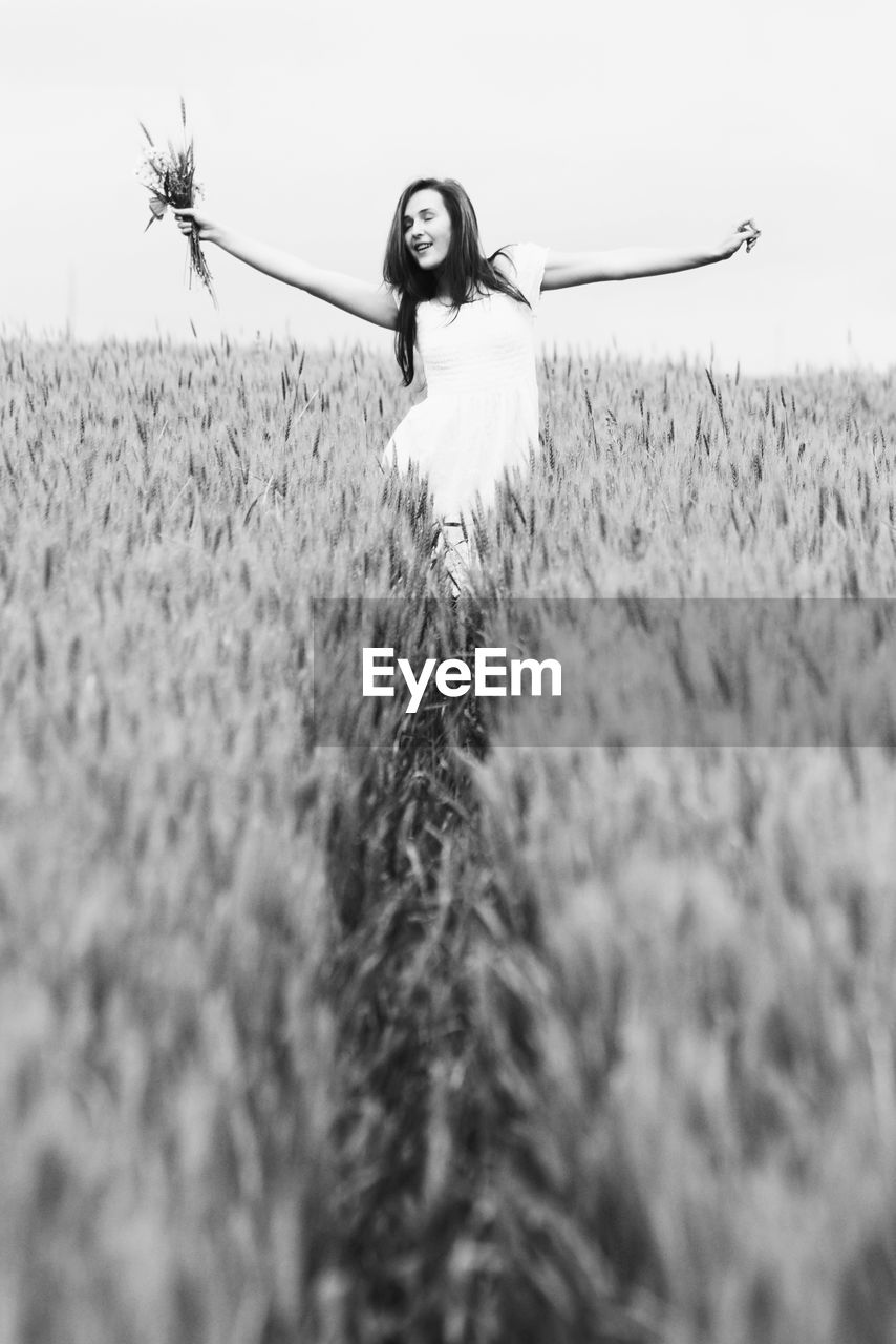 Young woman with arms outstretched standing at wheat farm