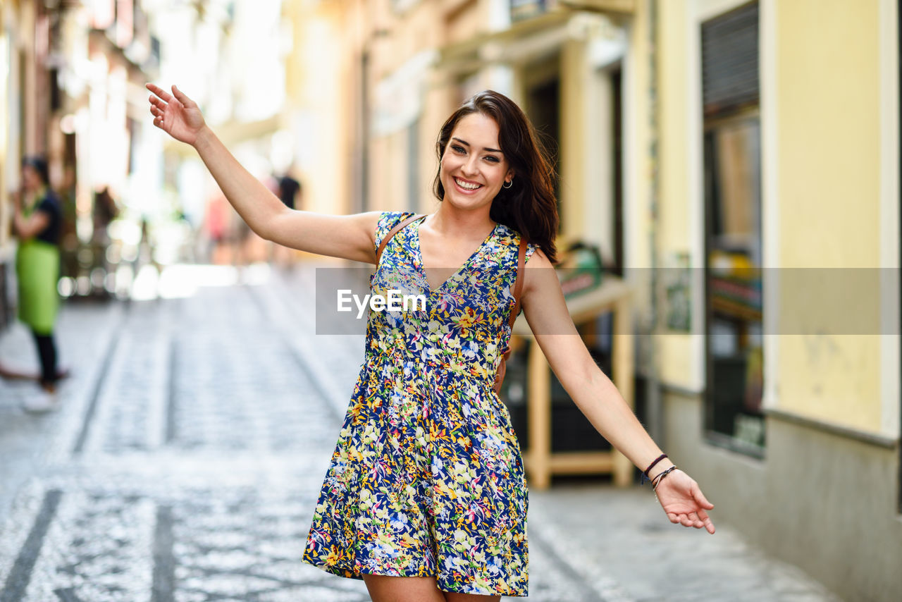 Portrait of happy woman standing with arms outstretched at street
