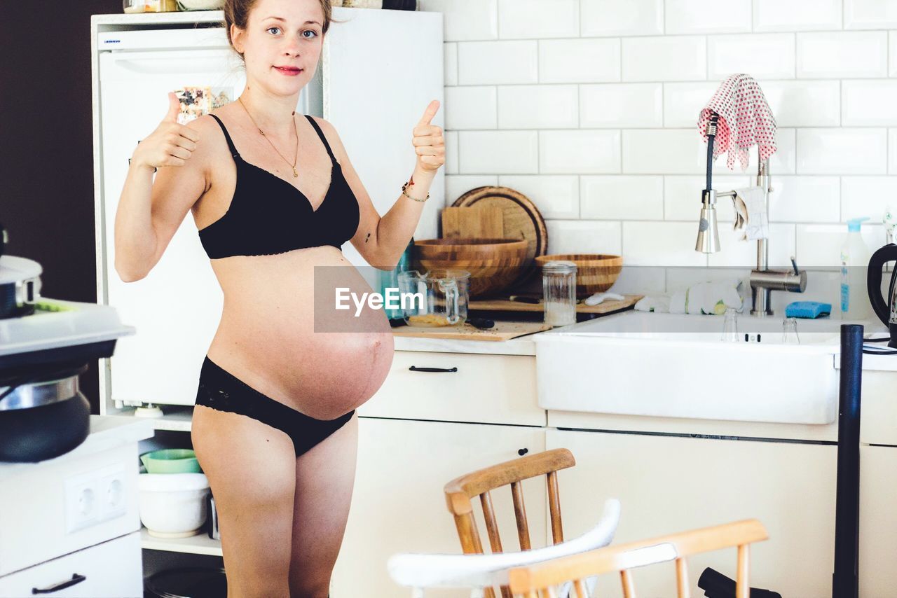 Portrait of pregnant woman gesturing while standing at home