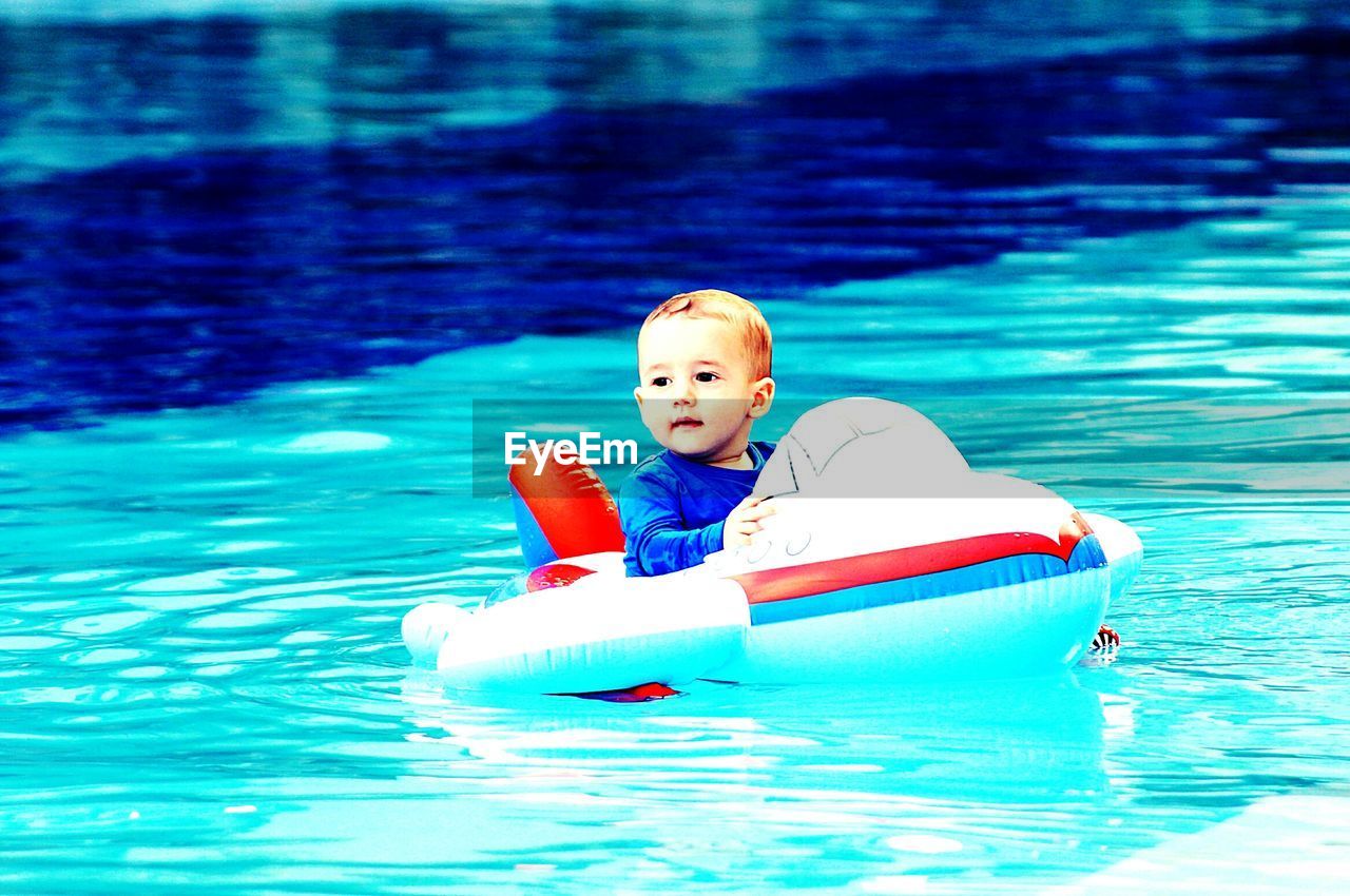 Cute baby boy sitting in inflatable ring at swimming pool