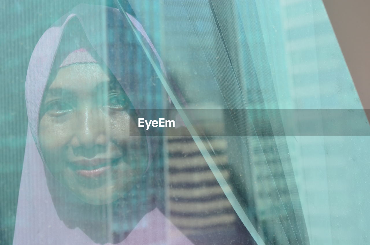 Portrait of woman wearing scarf seen through curtain