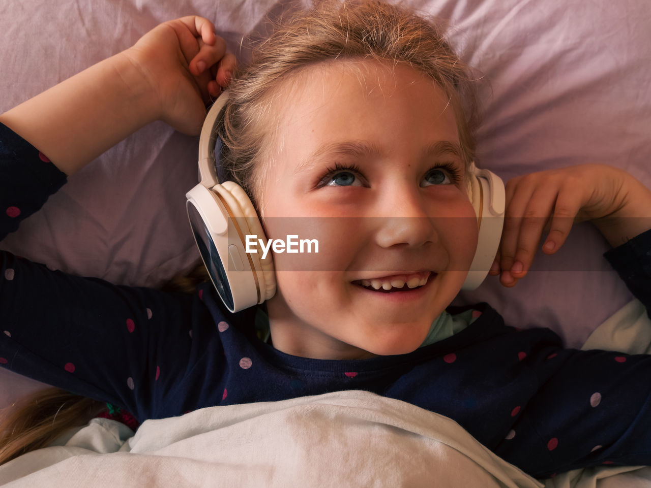 Child girl in headphones learns language listen to music podcast in smartphone online in bed at home