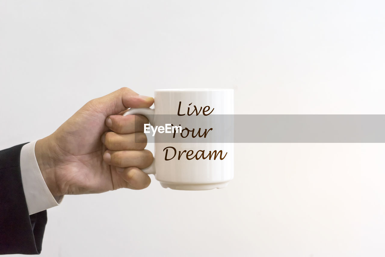 Close-up of hand holding coffee cup against white background