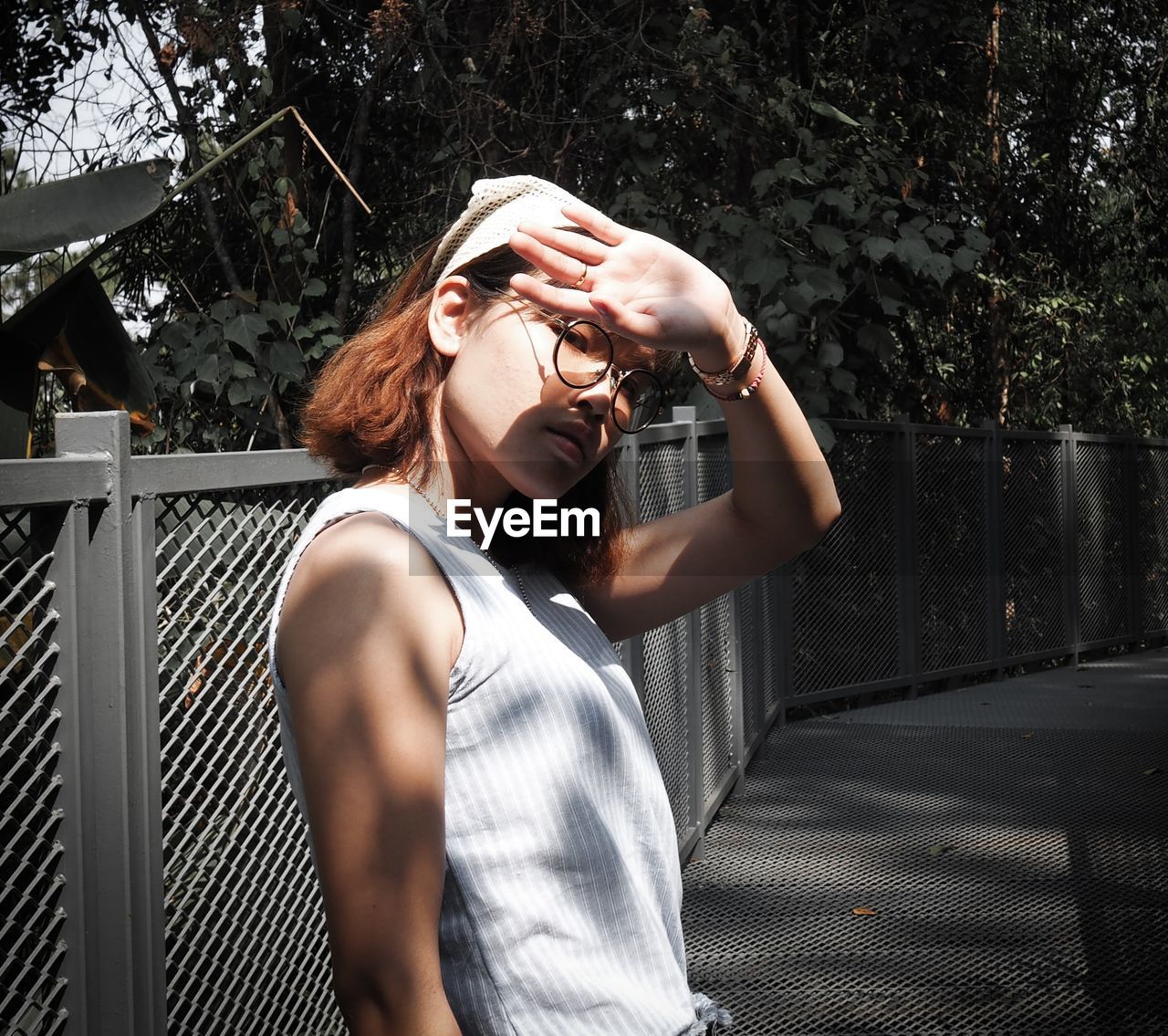 Portrait of young woman shielding eyes while standing on footpath