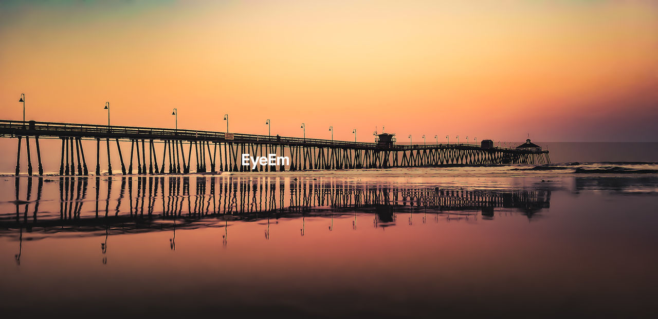 Silhouette pier on sea against orange sky