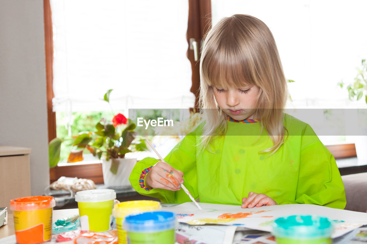 Girl painting on paper while sitting at home