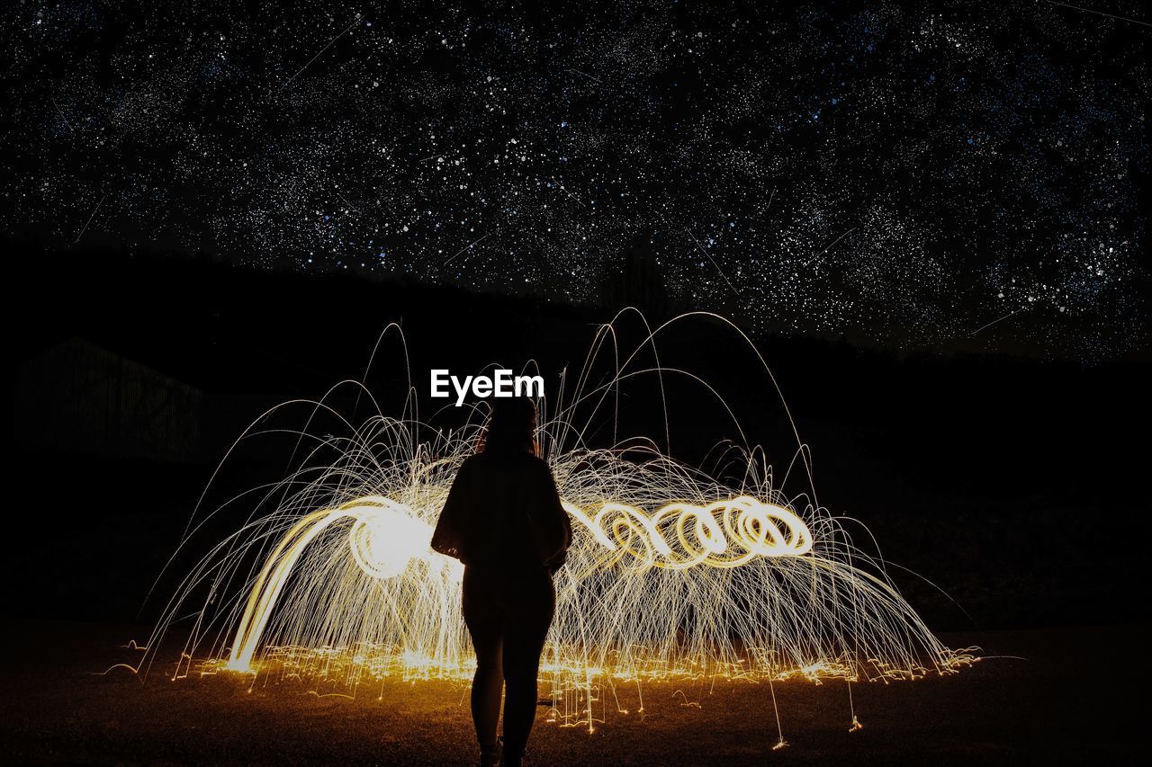 Rear view of woman standing by illuminated wire wool at night